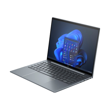 Angled view of a sleek, gray refurbished HP DRAGONFLY G4 laptop with a black keyboard, open to reveal its 13.5” touch display showing the Windows 11 home screen with blue abstract shapes on white; features include an Intel Core i7-1365U processor, 32GB DDR4 memory, and a 1TB NVMe SSD. - View 4
